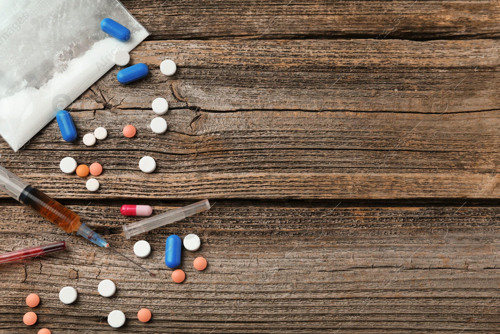 Photo of Drug addiction. Plastic bag with powder, syringes and pills on wooden table, flat lay. Space for text