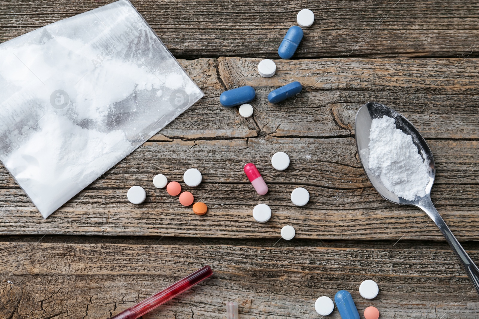 Photo of Drug addiction. Plastic bag with powder, spoon, syringe and pills on wooden table, flat lay