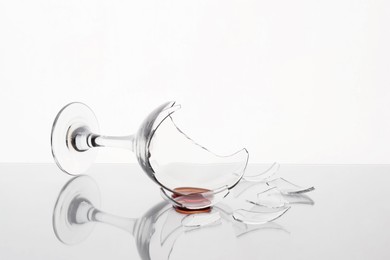 Photo of Pieces of broken glass with wine on table against white background