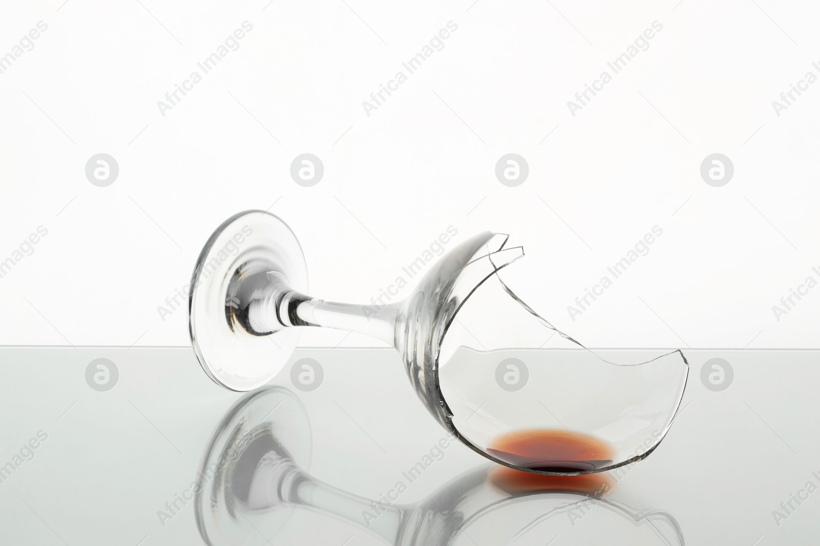 Photo of Piece of broken glass with wine on table against white background, closeup