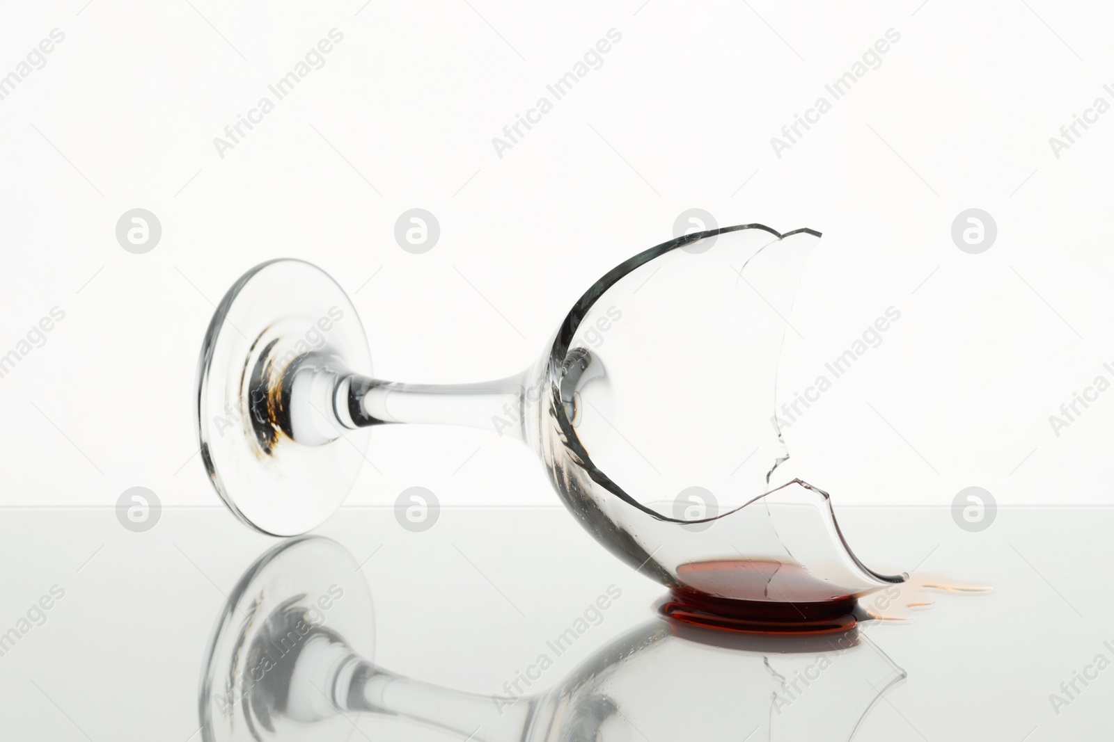 Photo of Broken glass with wine on table against white background, closeup