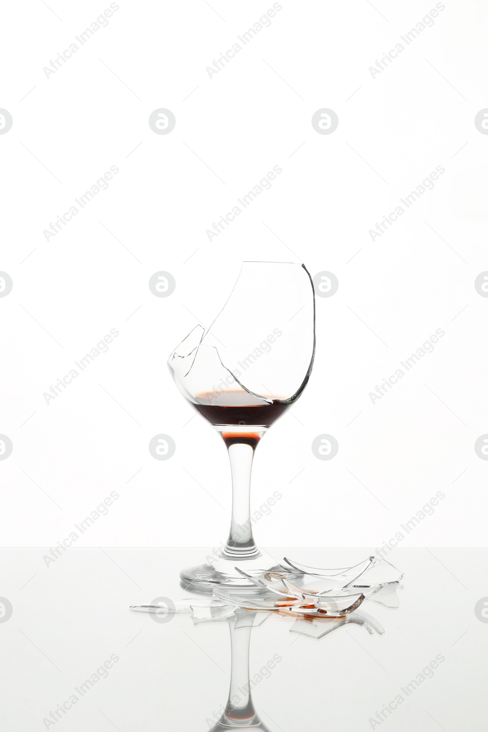 Photo of Pieces of broken glass with wine on table against white background