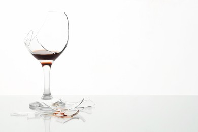 Photo of Pieces of broken glass with wine on table against white background, space for text