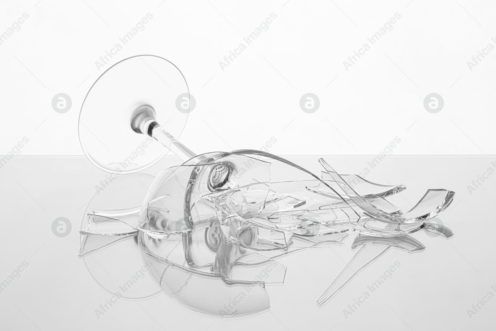 Photo of Pieces of broken wine glass on table against white background, closeup