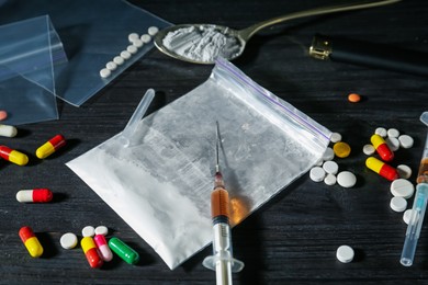 Photo of Drug addiction. Plastic bag with powder, syringes, pills and spoon on black wooden table, closeup