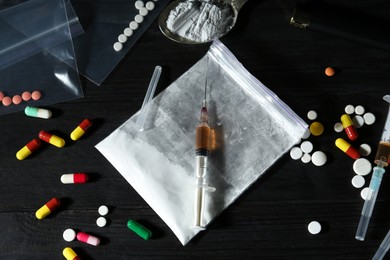 Photo of Drug addiction. Plastic bag with powder, syringes, pills and spoon on black wooden table, above view