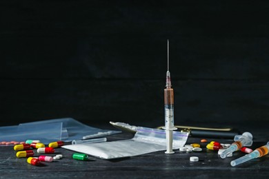 Photo of Drug addiction. Plastic bag with powder, syringes and pills on black wooden table, space for text