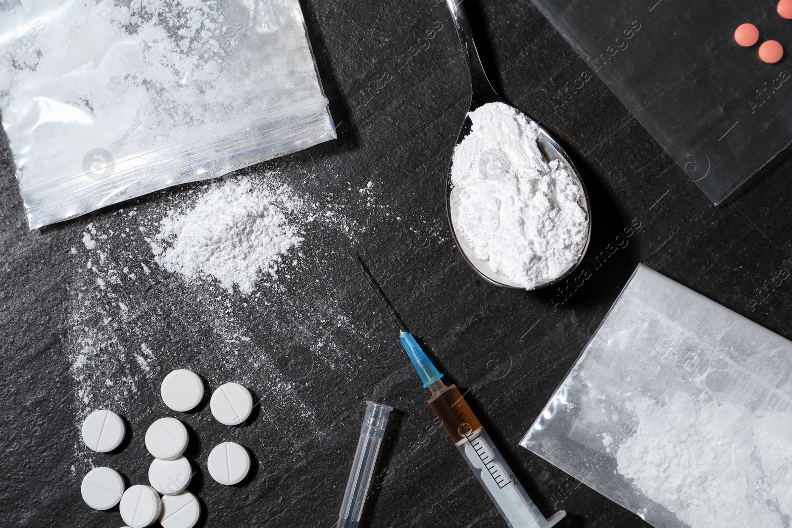 Photo of Drug addiction. Plastic bags with powder, spoon, syringes and pills on black textured table, flat lay