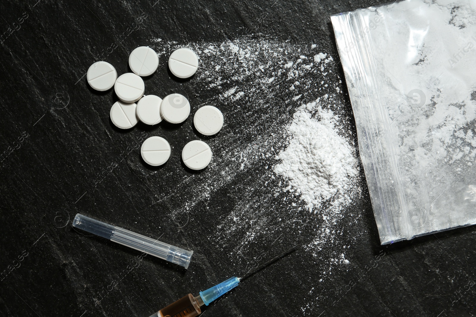 Photo of Drug addiction. Plastic bag with powder, syringe and pills on black textured table, flat lay