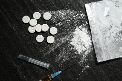 Photo of Drug addiction. Plastic bag with powder, syringe and pills on black textured table, flat lay