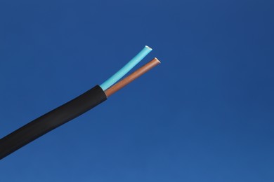 Photo of Black stripped electrical wire on blue background, closeup. Space for text