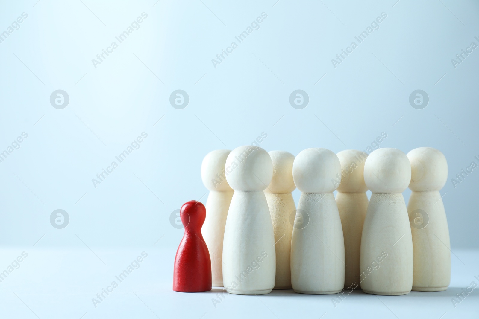 Photo of Human resources concept. Red figure in front of wooden ones on light background, closeup. Space for text