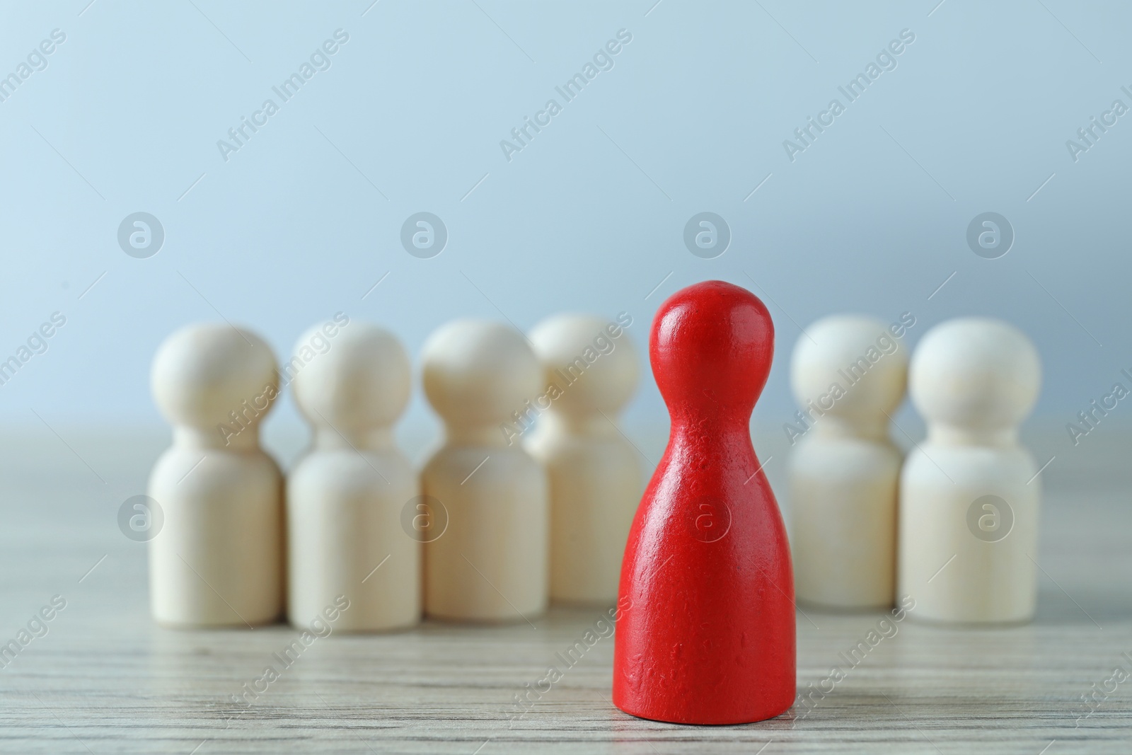 Photo of Human resources concept. Red figure in front of wooden ones on table against light background, closeup