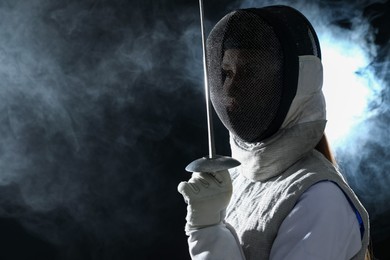 Photo of Fencer with epee in smoke on black background, space for text