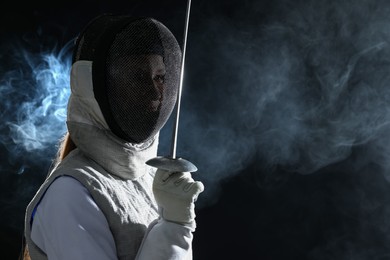 Photo of Fencer with epee in smoke on black background, space for text