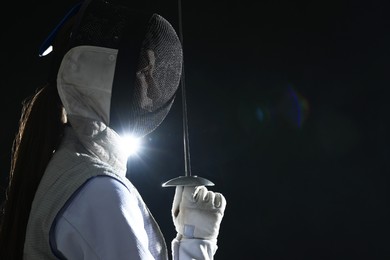 Photo of Fencer with epee on dark background, space for text