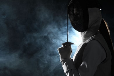 Photo of Fencer with epee in smoke on black background, space for text