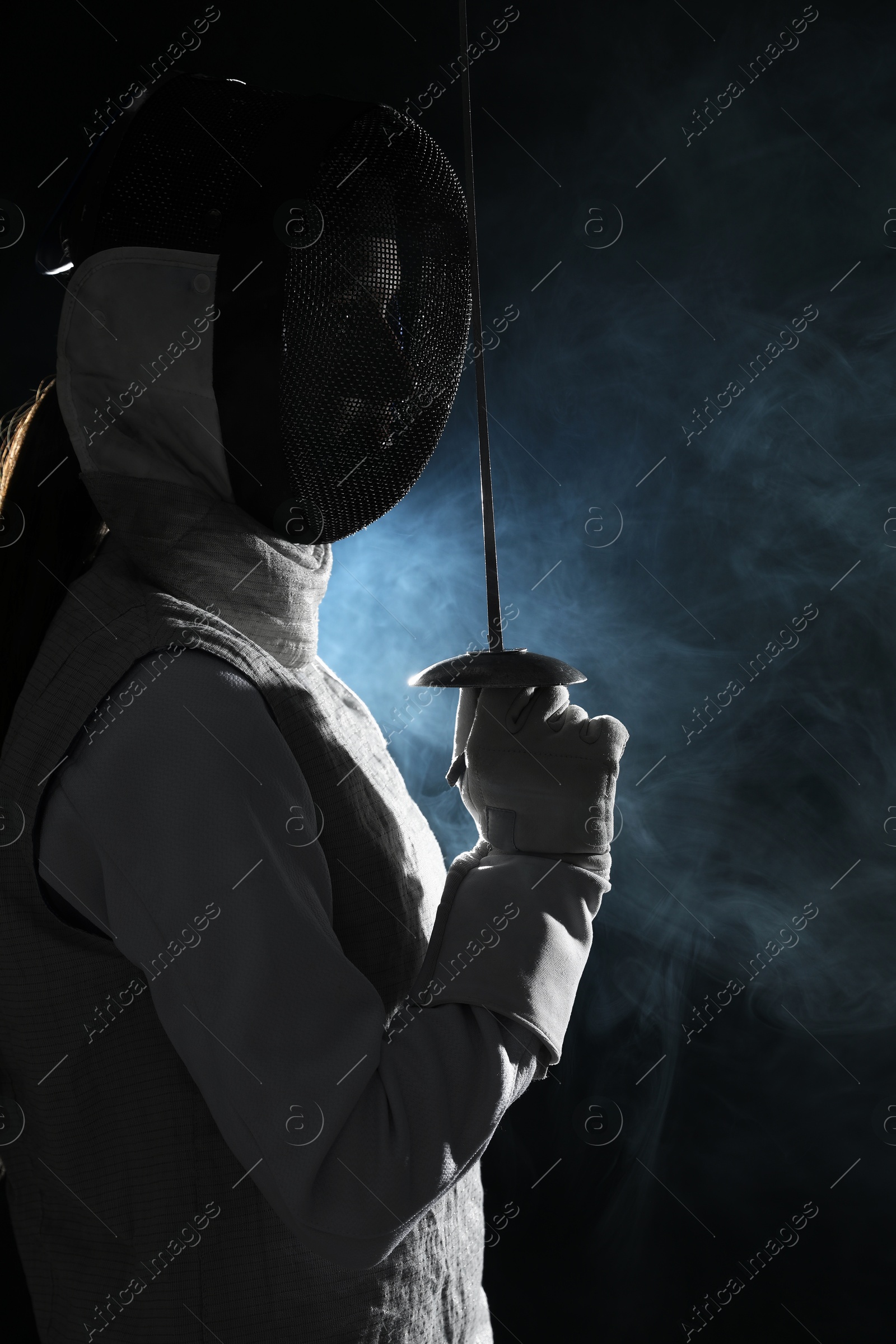 Photo of Fencer with epee in smoke on black background