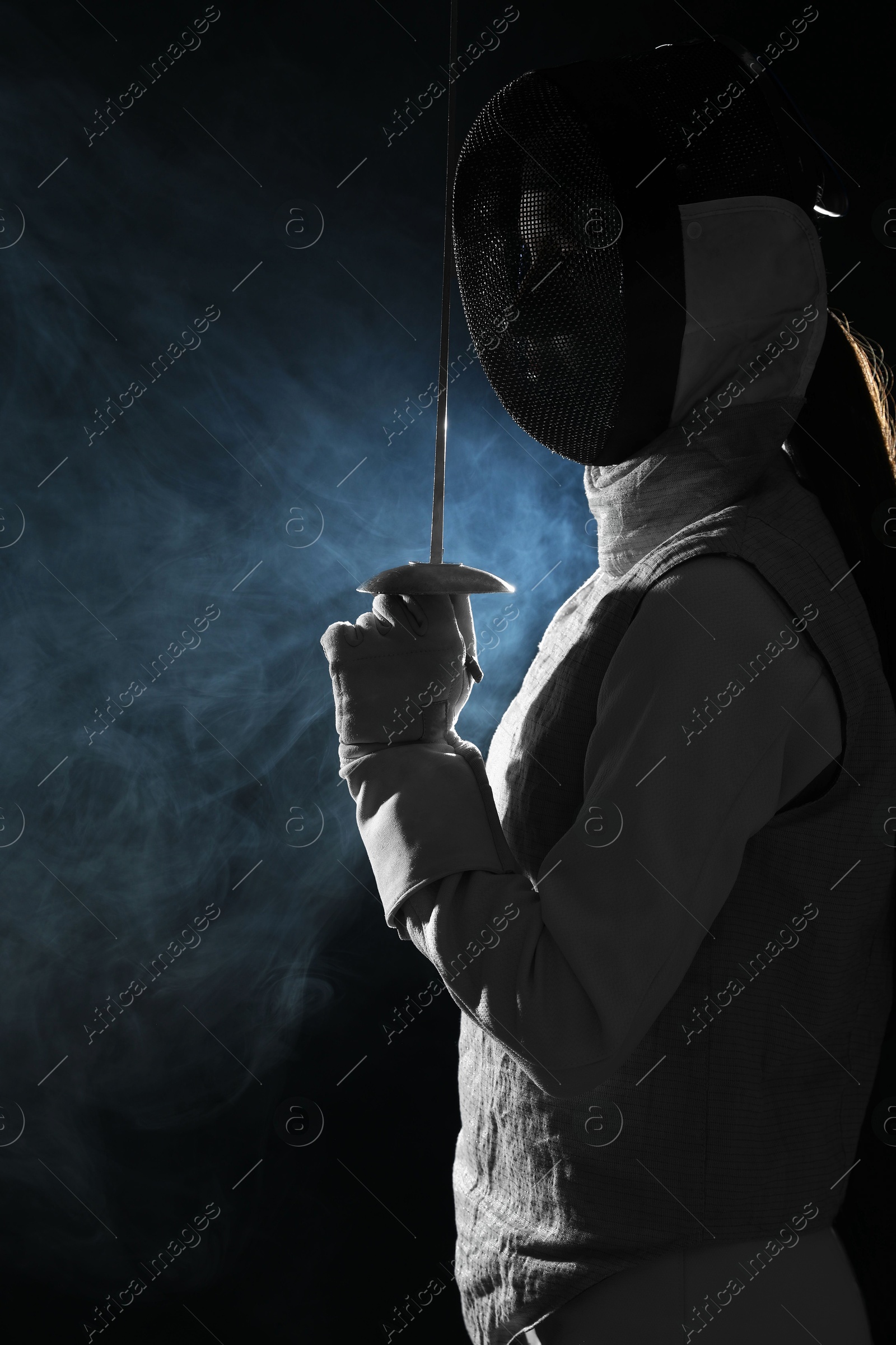 Photo of Fencer with epee in smoke on black background