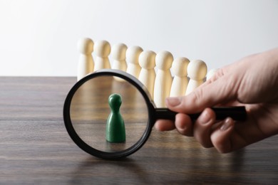 Photo of Human resources concept. Woman with magnifying glass and wooden pieces at table, closeup