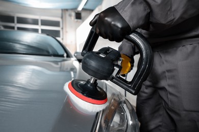 Photo of Man polishing car hood with orbital polisher indoors, closeup