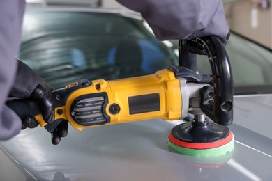 Photo of Man polishing car hood with orbital polisher indoors, closeup