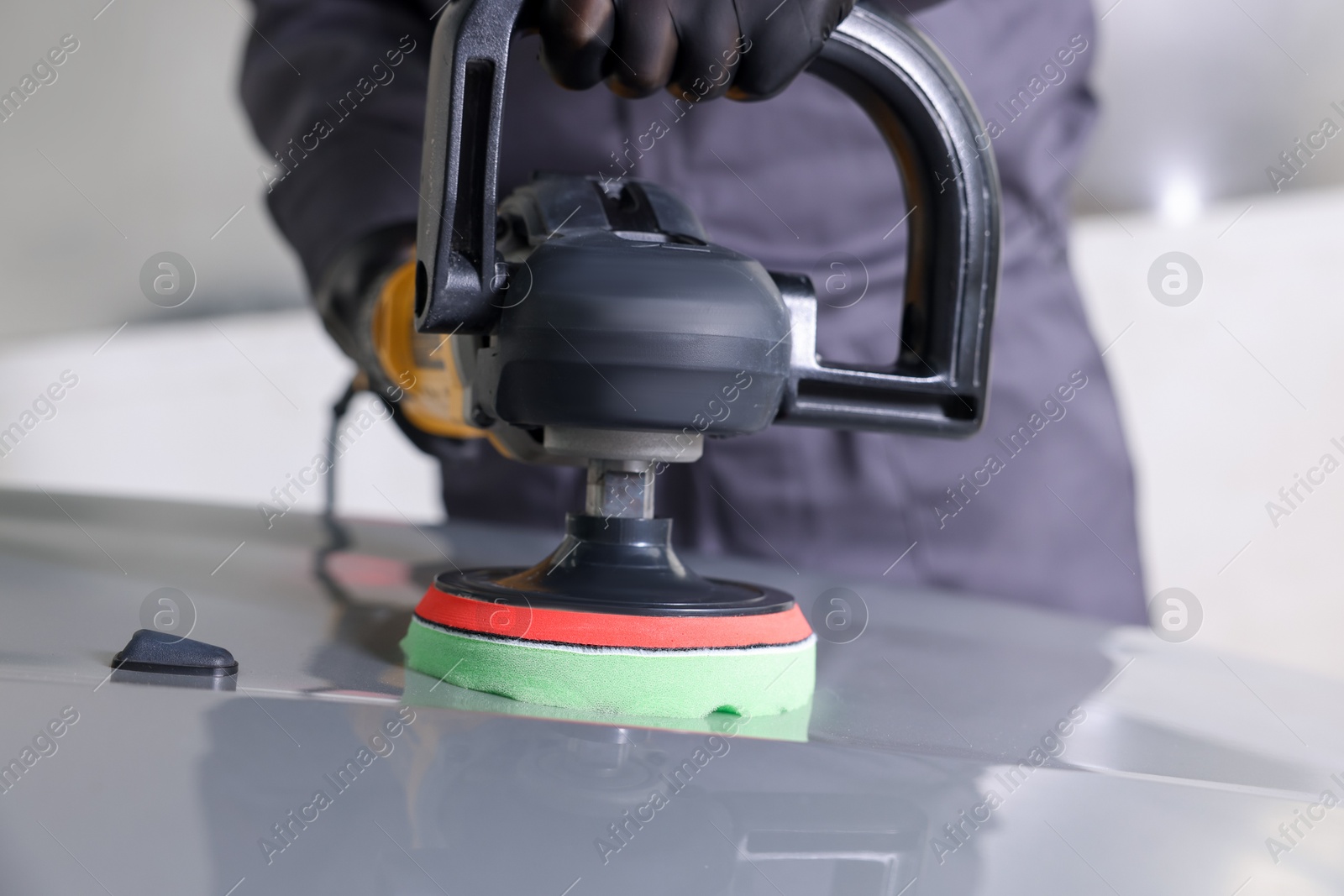 Photo of Man polishing car hood with orbital polisher indoors, closeup