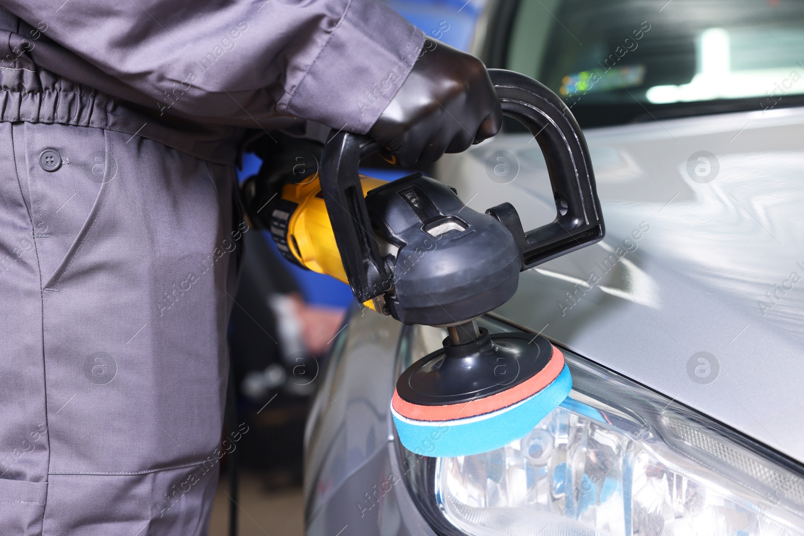 Photo of Man polishing car headlight with orbital polisher indoors, closeup