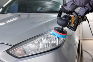 Photo of Man polishing car headlight with orbital polisher indoors, closeup