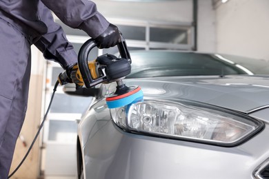 Photo of Man polishing car headlight with orbital polisher indoors, closeup