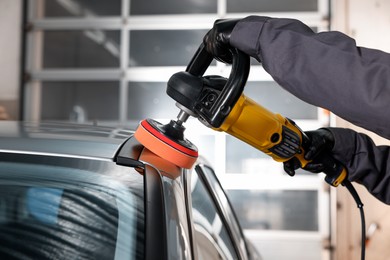 Photo of Man polishing car with orbital polisher indoors, closeup