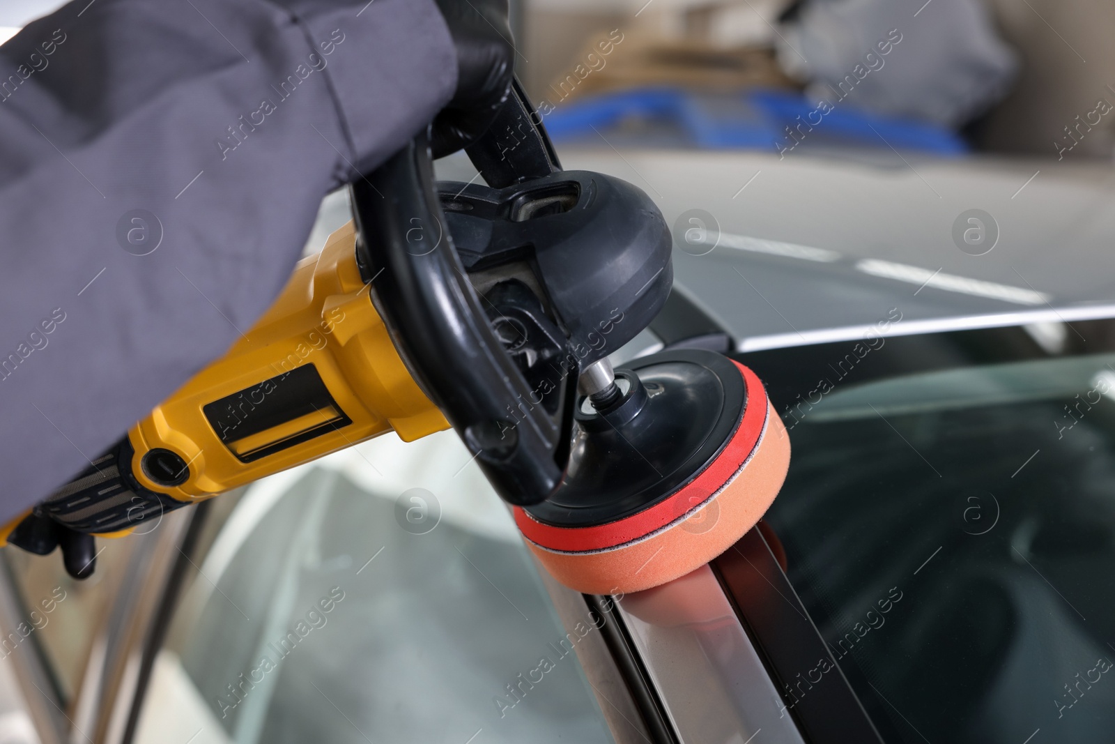 Photo of Man polishing car with orbital polisher indoors, closeup