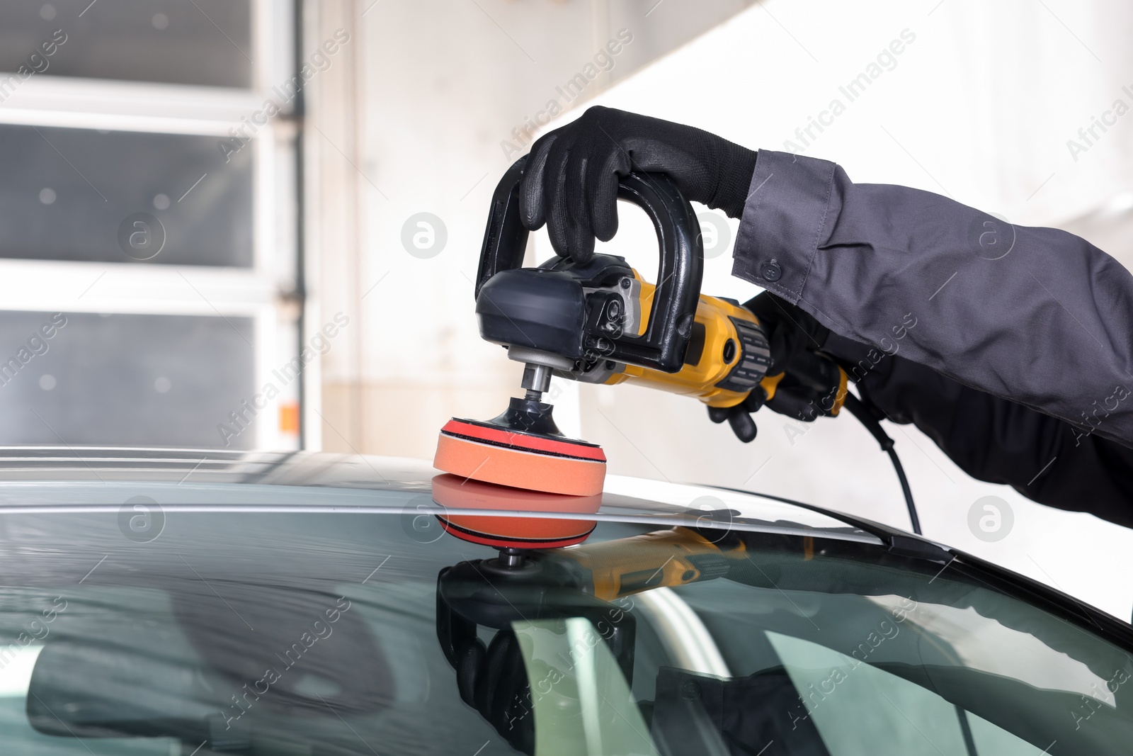 Photo of Man polishing car with orbital polisher indoors, closeup