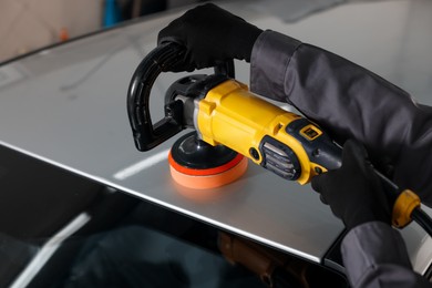 Photo of Man polishing car with orbital polisher indoors, closeup