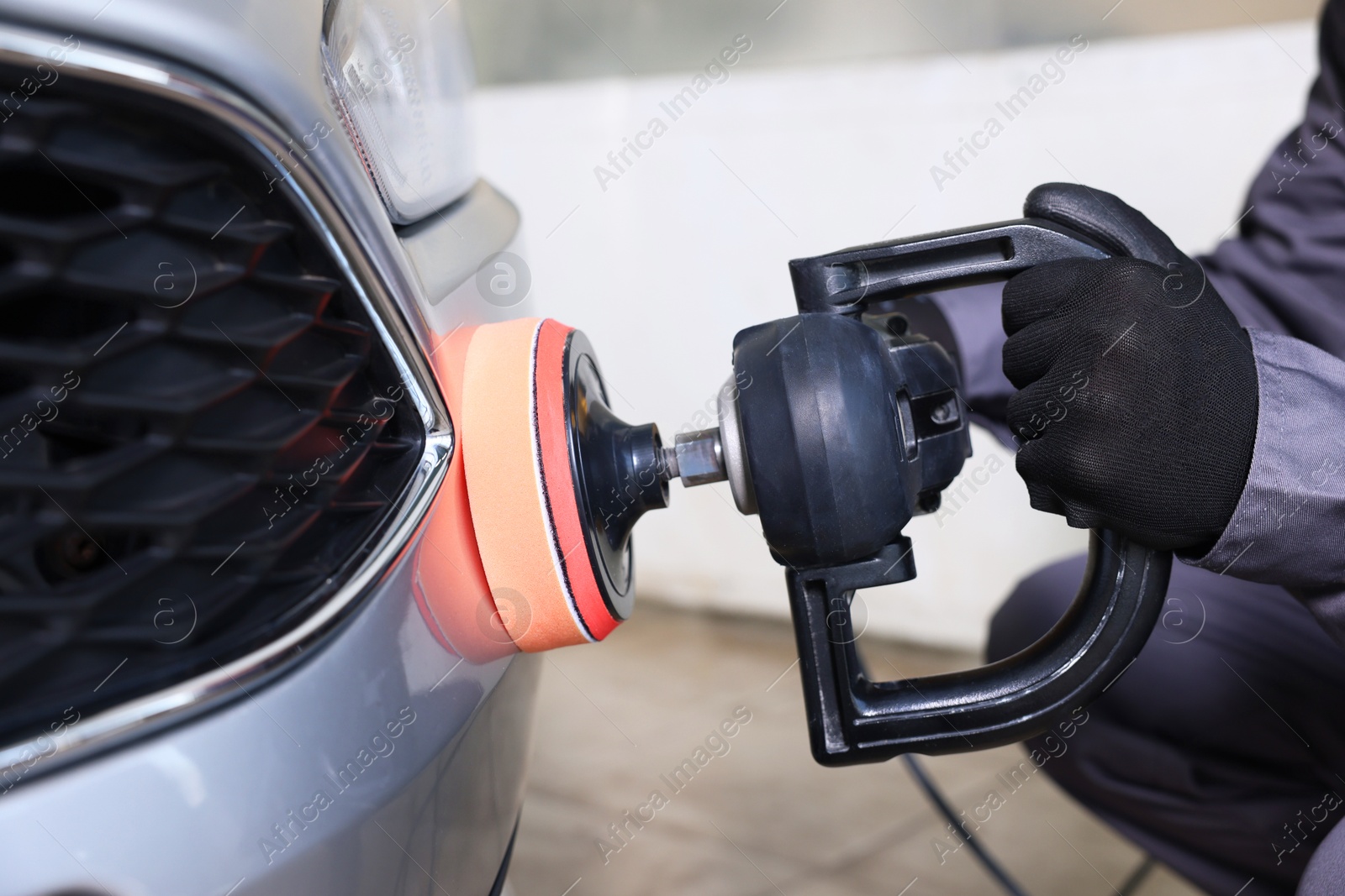 Photo of Man polishing car with orbital polisher indoors, closeup