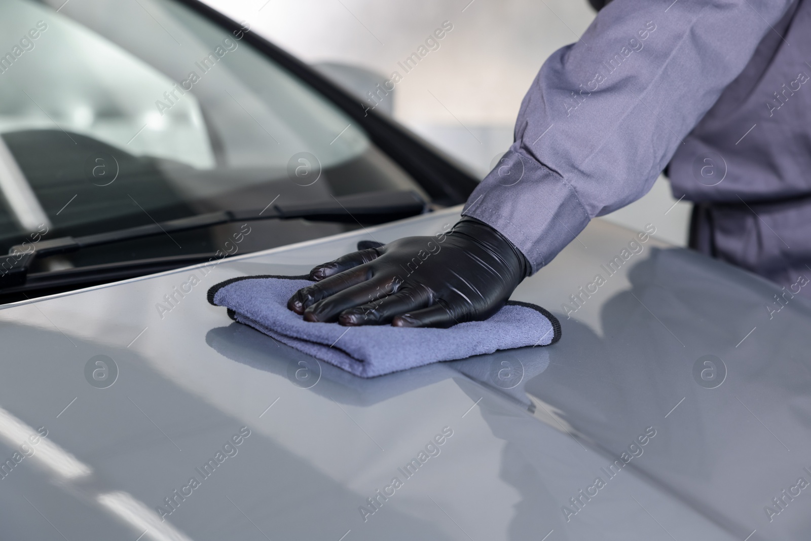 Photo of Man polishing car hood with rag indoors, closeup