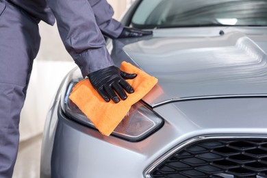 Photo of Man polishing car headlight with orange rag indoors, closeup