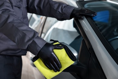 Photo of Man cleaning car side view mirror with yellow rag indoors, closeup