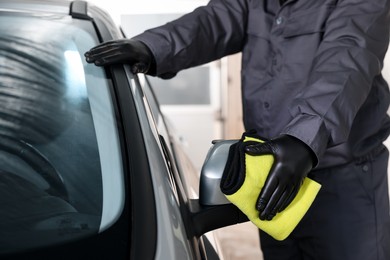 Photo of Man cleaning car side view mirror with yellow rag indoors, closeup