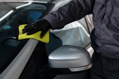 Photo of Man polishing car with yellow rag indoors, closeup