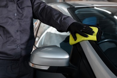 Photo of Man polishing car with yellow rag indoors, closeup