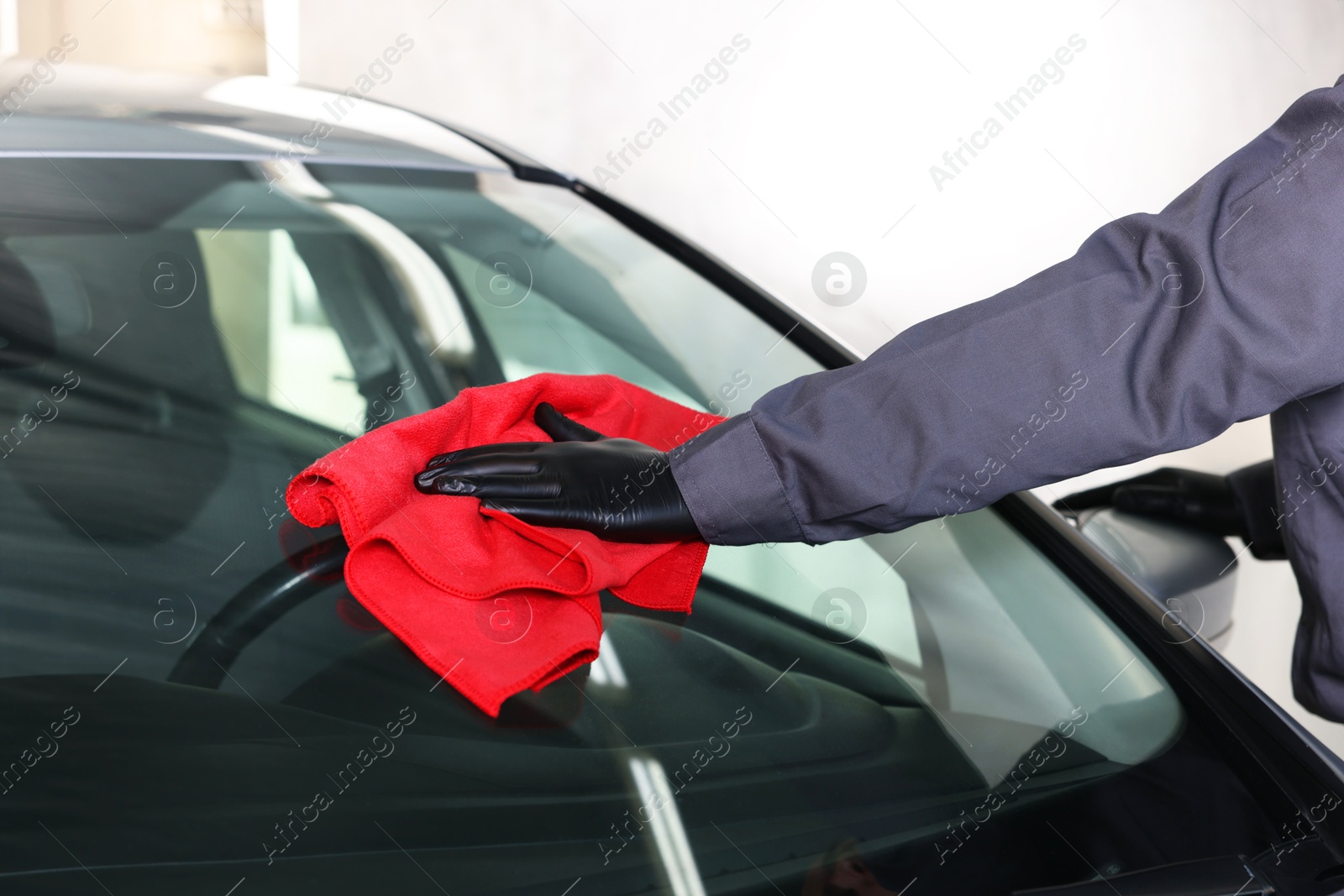 Photo of Man polishing car windshield with red rag indoors, closeup