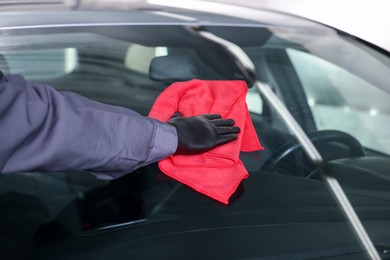 Photo of Man polishing car windshield with red rag indoors, closeup