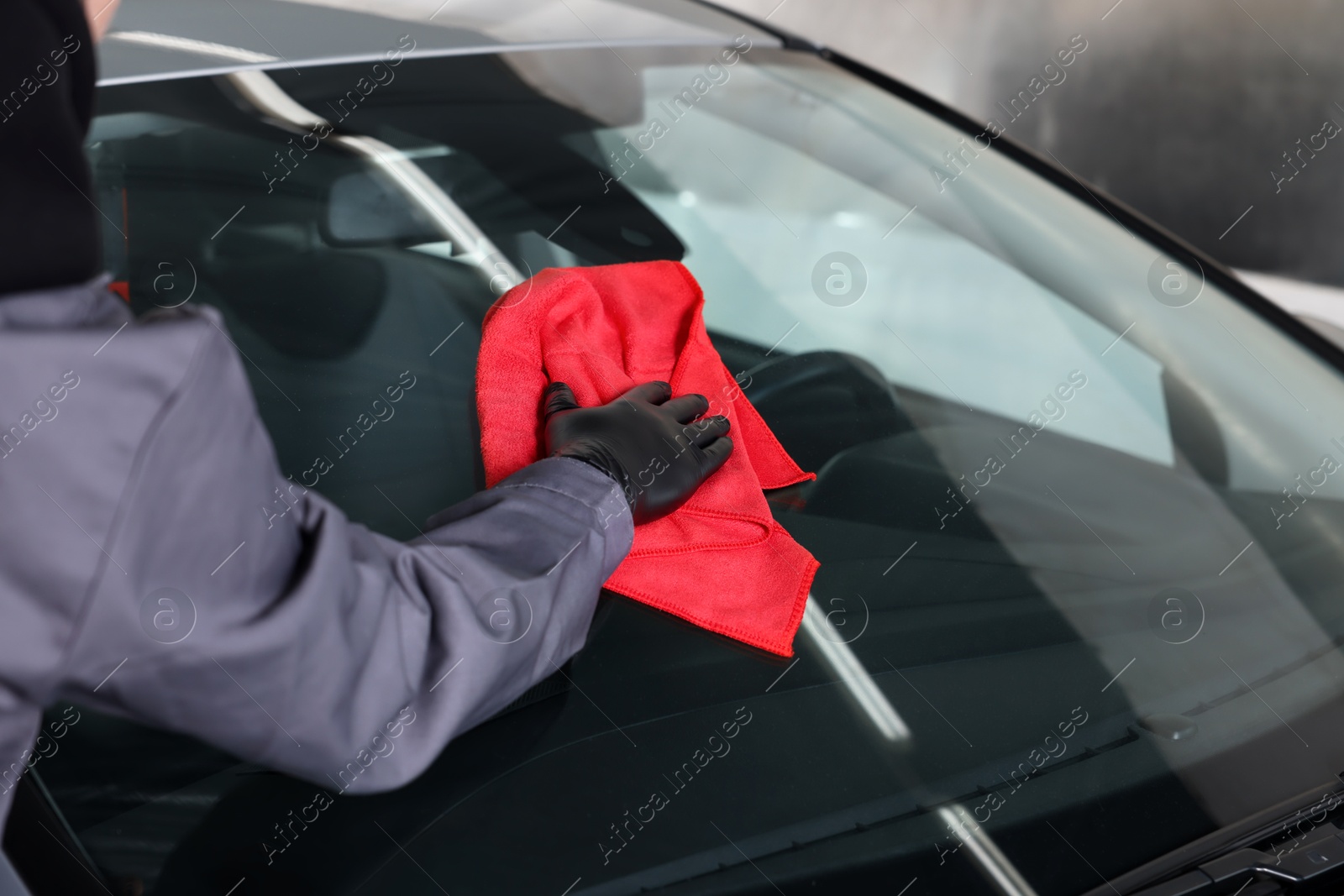 Photo of Man polishing car windshield with red rag indoors, closeup