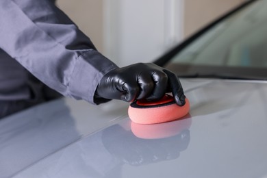 Photo of Man polishing car hood with sponge indoors, closeup