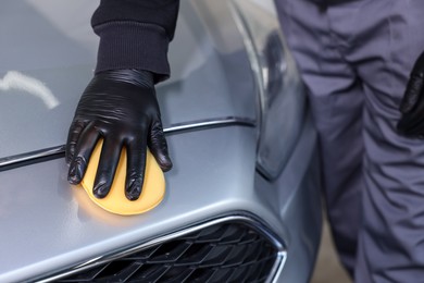 Photo of Man polishing car hood with yellow sponge indoors, closeup