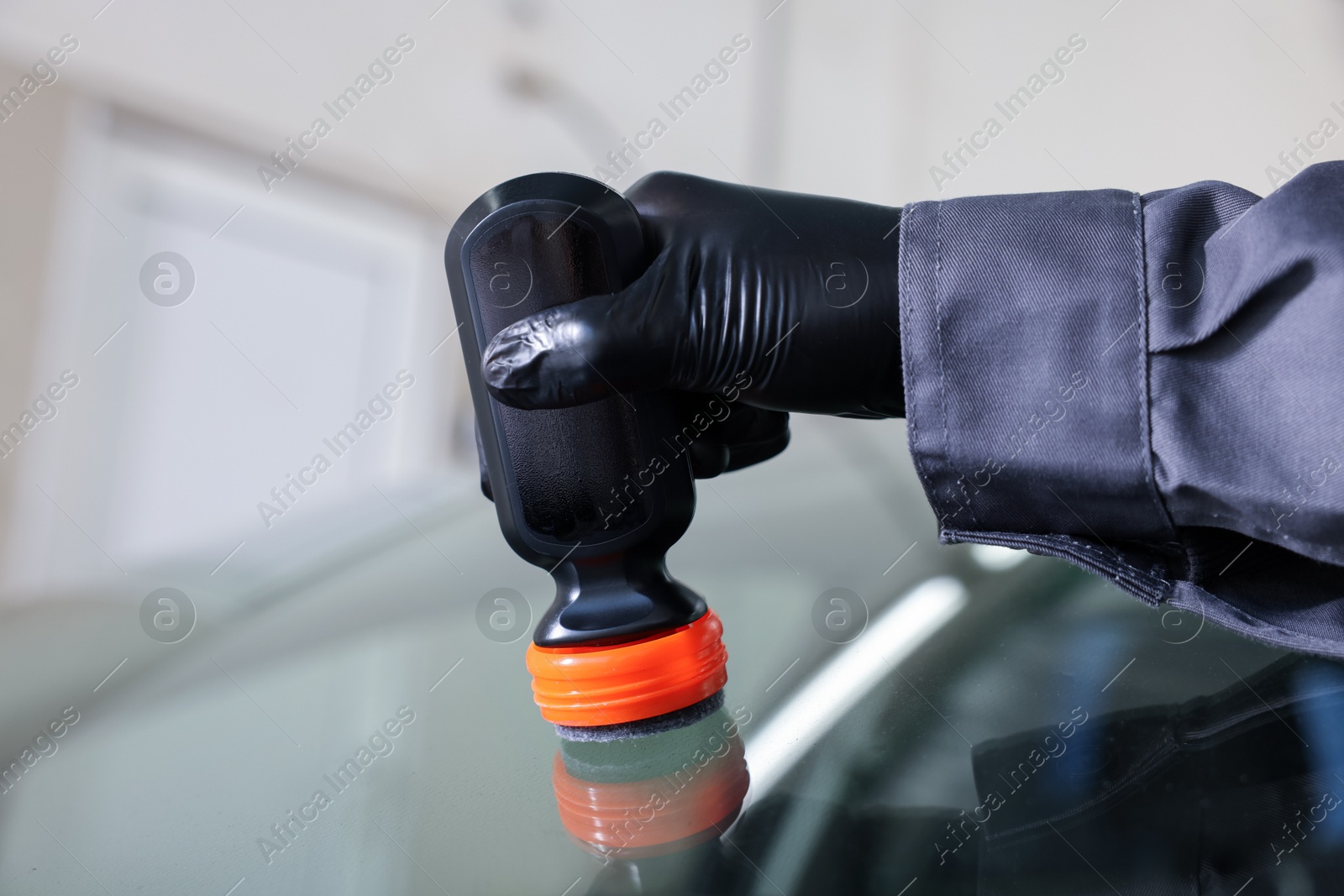 Photo of Man polishing car windshield indoors, closeup view