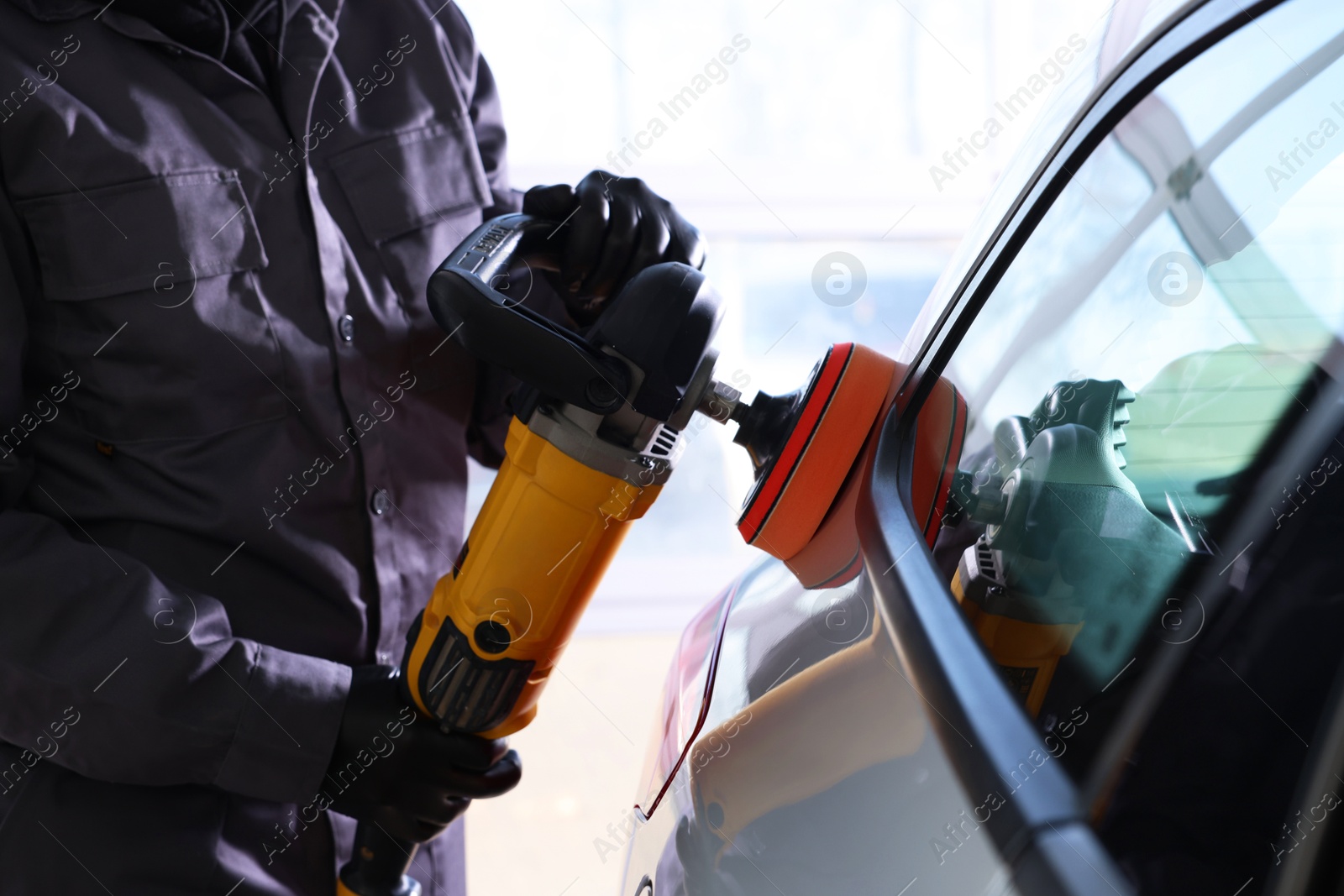 Photo of Man polishing car with orbital polisher indoors, closeup