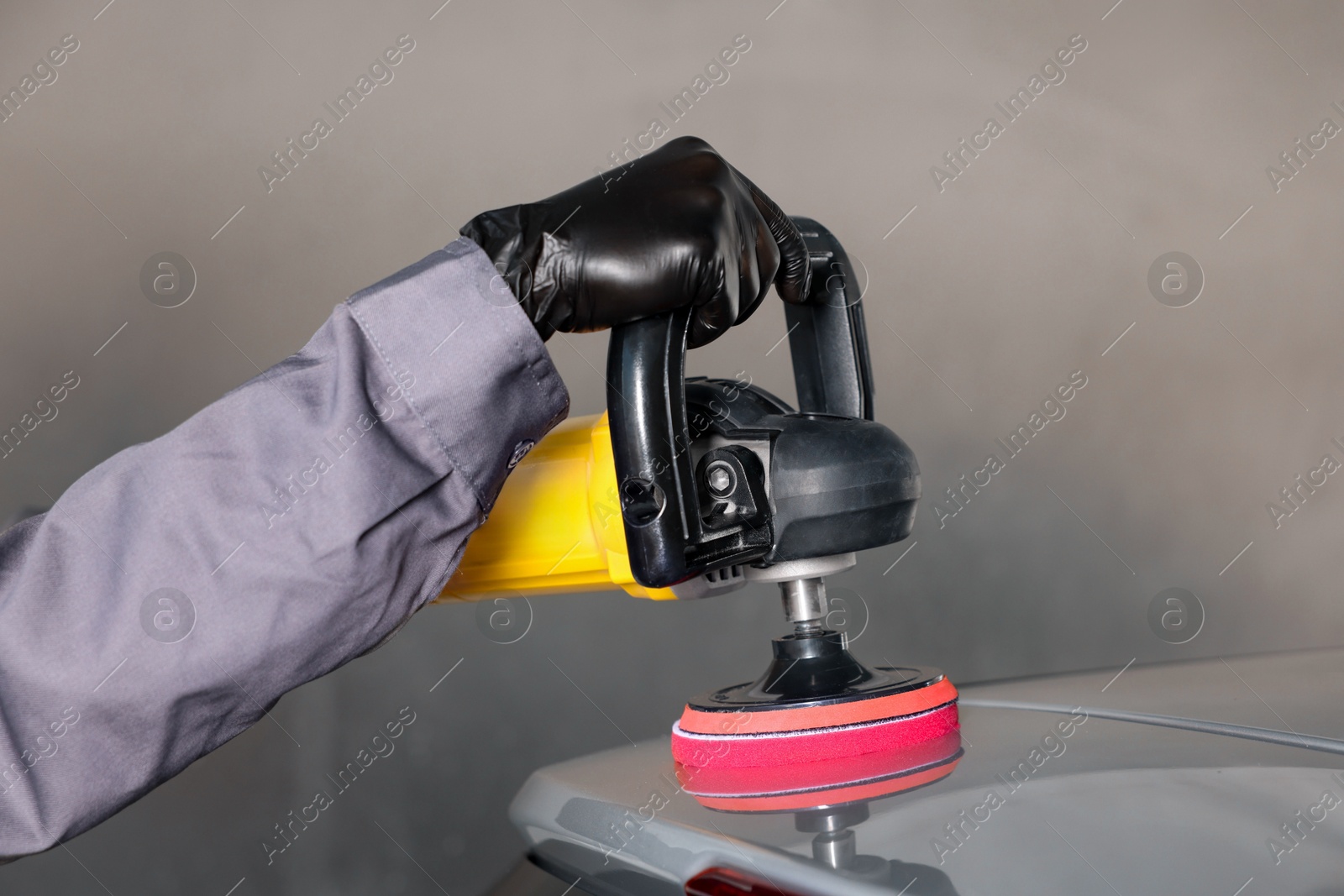 Photo of Man polishing car with orbital polisher indoors, closeup