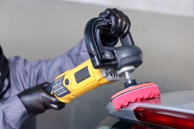 Photo of Man polishing car with orbital polisher indoors, closeup